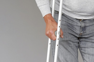Man on crutches on a gray background. Close-up a elderly man walking with crutches.