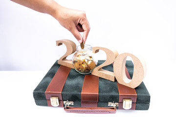 Hand putting coin into glass piggy bank with 2020 character, set business goals with New Year 2020