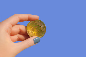 Woman hand holding gold bitcoin/cyptocurrency isolated on blu background, close up.  Finance concept