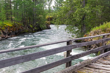 Fototapeta na wymiar Old wooden bridge over the fast river.