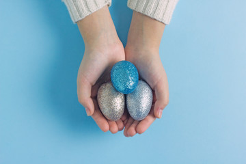 Easter eggs in hands on a blue background. Close-up of a child's hands holding colored eggs of blue, silver and gold color. View from above. Easter background.