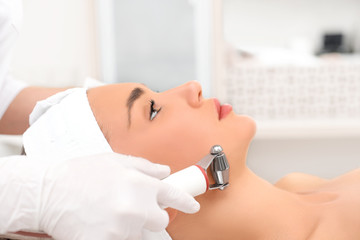 woman close up receiving electric facial massage on microdermabrasion equipment at beauty salon.