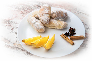 food croissants sprinkled with powdered sugar with sliced oranges with cinnamon star anise on a white plate on a light background
