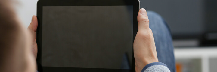 Male hand holds tablet in home setting while