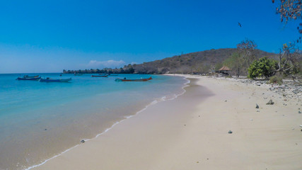 An areal, drone shot with a view on an idyllic Pink Beach on Lombok, Indonesia. Many boats drifting on a calm surface of the sea. Unspoiled, hidden gem. Perfect place for peaceful, relaxed holidays