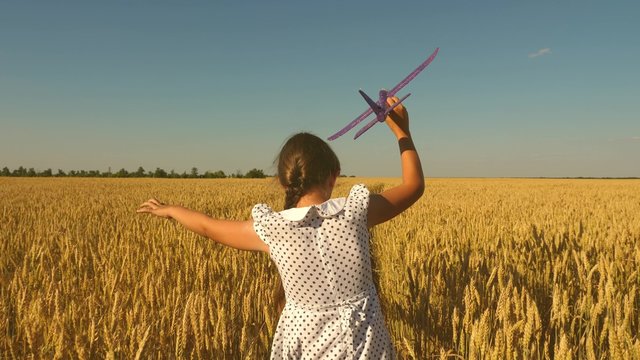 Happy girl runs with a toy airplane on a field in the sunset light. children play toy airplane. teenager dreams of flying and becoming a pilot. girl wants to become a pilot and astronaut. Slow motion