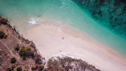 A drone shot of a  couple lying on the Pink Beach in Lombok, Indonesia. A hidden gem, not spoiled by tourists. Solitude and calmness. Waves gently spreading on the beach. Happiness while travelling