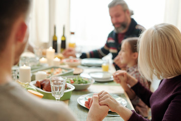 Young man, his mature mother and the rest of family holding by hands by table