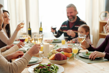 Hand of young man holding glass of wine over served table during toast at dinner