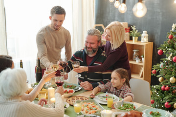 Happy mature and young couples toasting with glasses of wine over served table