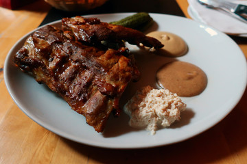 baked ribs served on a white plate with cucumber horseradish and mustard in a restaurant