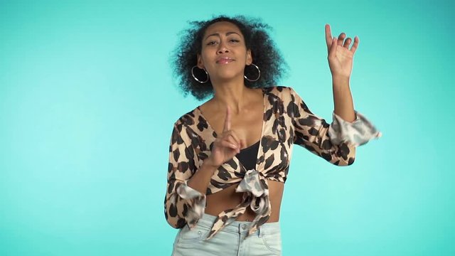 Beautiful african american woman with afro hair having fun smiling and dancing in studio against blue background. slow motion