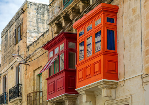 Two traditional Maltese enclosed wooden balconies painted in red and orange in Cospicua (Bormla), Malta. Authentic Maltese urban scene.