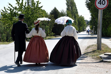 A man and a woman walked along the road, arm in arm, in nineteenth-century clothing.