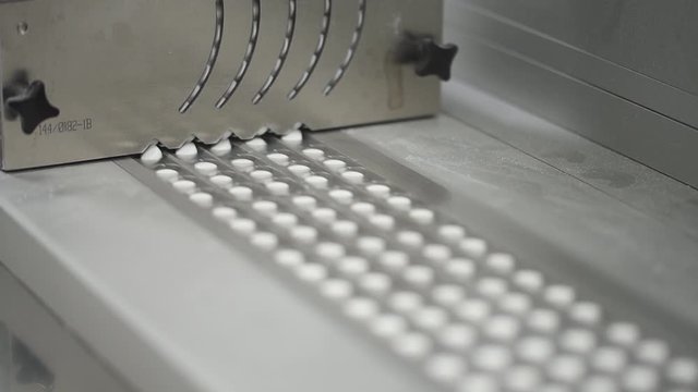 Tablets in blisters go on a conveyor belt. Automated packing at drug production. Closeup shot of an automated pill packaging machine. Pharmaceutical machinery for medicine manufacturing