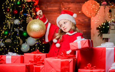 Fototapeta na wymiar Magic glass ball makes her feel the unique atmosphere of Christmas. Small child holding christmas glitter ball. Little girl looking at ornament ball. Cute kid with golden christmas ball