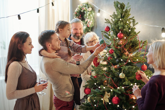 Young man with little daughter and other family members standing by xmas tree