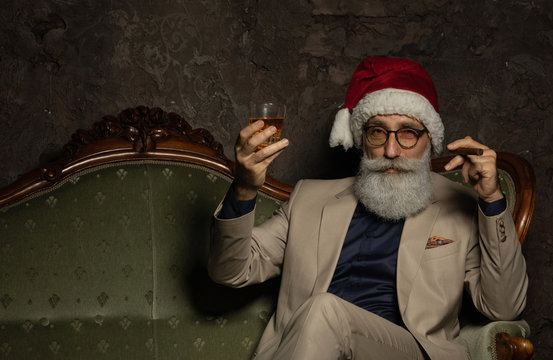 Santa claus boss drinking brandy and smoking a cigar. Businessman in elegant suit in santa hat. Rich Xmas concept.