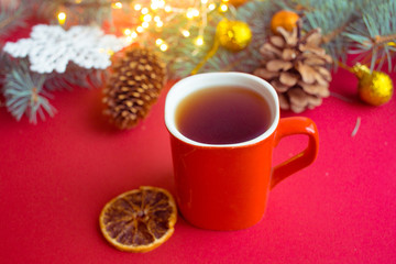 Fototapeta na wymiar red cup with hot tea on a red background with dried orange and cones. Christmas card.