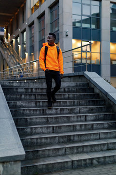 african-american man in stylish orange hoodie sweatshirt with backpack goes down stairs