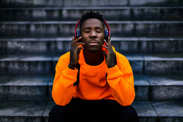 african-american man in stylish orange hoodie sweatshirt in wireless headphones listening music and...