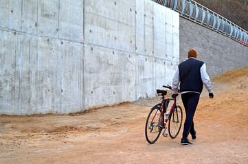 Man pushing his bike through the park. Gray concrete wall background.