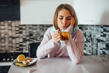 Young ill woman with cup of hot tea at home kitchen.