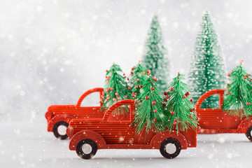 Small toy cars carring christmas tree on blue background with snow . Sesonal holidays, greeting card, christmas mood concept.