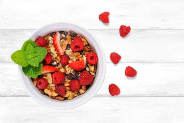 Top view of a homemade organic granola with oats, nuts, raspberries and strawberries in a white bowl on a wooden vintage tabel