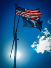 US Flag flying over South carolina state flag waving in wind on a sunny day in front of blue sky