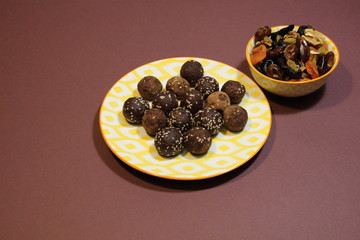 Energy balls dessert in colorful plate made of dried fruits, cocoa, sesam seeds on brown background