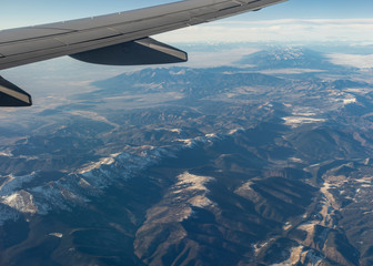 Obraz premium Looking out the window of an airplane soaring high above the scenic vista of the Rocky Mountains in the United States.