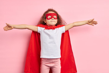 Curly caucasian kid imagine that she is blasting off as superhero, portrait, isolated pink...