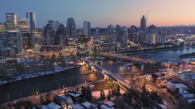 Aerial: Hyperlapse timelapse establishing shot of the Calgary city skyline at night. In the foreground is the Peace Bridge & the Bow River