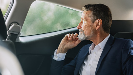 Side view of mature businessman sitting on a backseat of a car and looking out of window