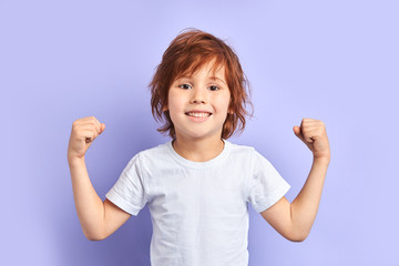 Cute caucasian kid wearing white t-shirt shows how he is strong and powerful, idolated over purple...