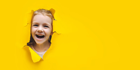 The little girl smiles happily and looks up through the hole in the yellow paper. The concept of...
