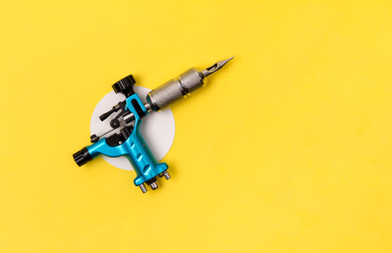 Blue tattoo machine on yellow background. Tattooing artist studio minimal layout