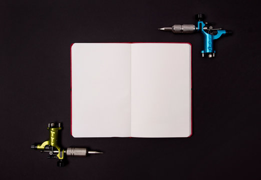 Tattoo machines with notepad on black background. Tattooing artist studio template