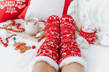 Woman in socks on White Christmas background with cups of cocoa drink and  christmas presents. Cozy winter holidays