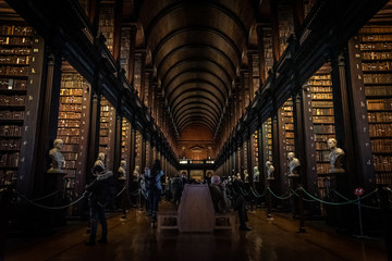 Naklejka premium DUBLIN, IRLANDIA, 21 grudnia 2018: Długi pokój w bibliotece Trinity College, gdzie znajduje się Księga z Kells. Widok perspektywiczny miejsca z dużą ilością książek i posągów na skrzyni.