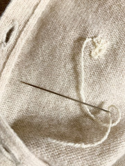 Expensive cashmere sweater with holes caused by cloth moths (Tineola bisselliella) is being repaired with a needle. Selective focus