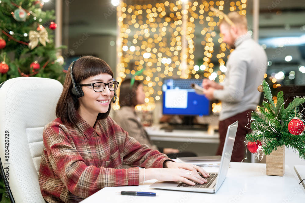 Poster pretty brunette operator with headset typing in front of laptop on xmas day
