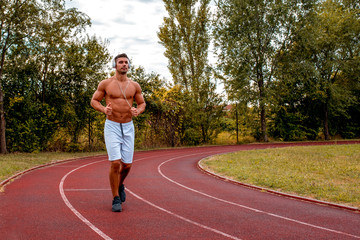 Portrait of athlete man with headphones jogging on a track