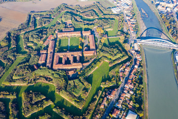 Aerial view of walls and bastions of modern six-star hexagon shaped fort Cittadella of Alessandria on winding river Tanaro. Piedmont, Italy. Bridge Ponte Meier connects fortress to town centre - obrazy, fototapety, plakaty