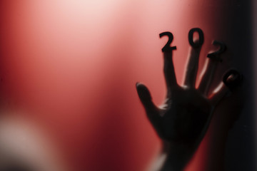 silhouette of a female hand with date on fingers pressed to glass of door with a red strange backlight, destruction of the stereotype happy new year, entering 2020 horror genre