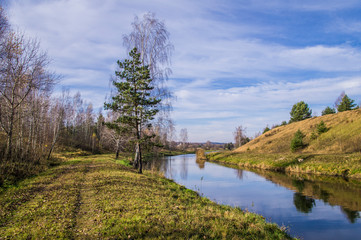 A forest river flows through a field and hills.