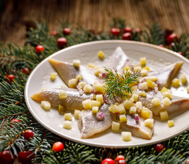 Fototapeta na wymiar Christmas Herrings fillets with apples, pickled cucumbers, red onion and spices on a ceramic plate on a festive decorated wooden table, close-up. Christmas, traditional dish