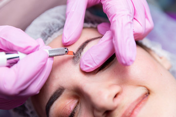 Obraz na płótnie Canvas Cosmetic procedures for the treatment of eyebrows. Microblading in the beauty salon. Professional cosmetology. The process of applying the pigment.
