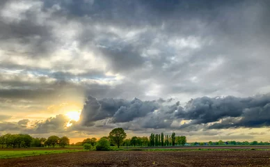 Fotobehang Colorful countryside sunrise or sunset over the agraric farmfields showing the dramatic colors and stormy clouds in the dark sky  © Bjorn B